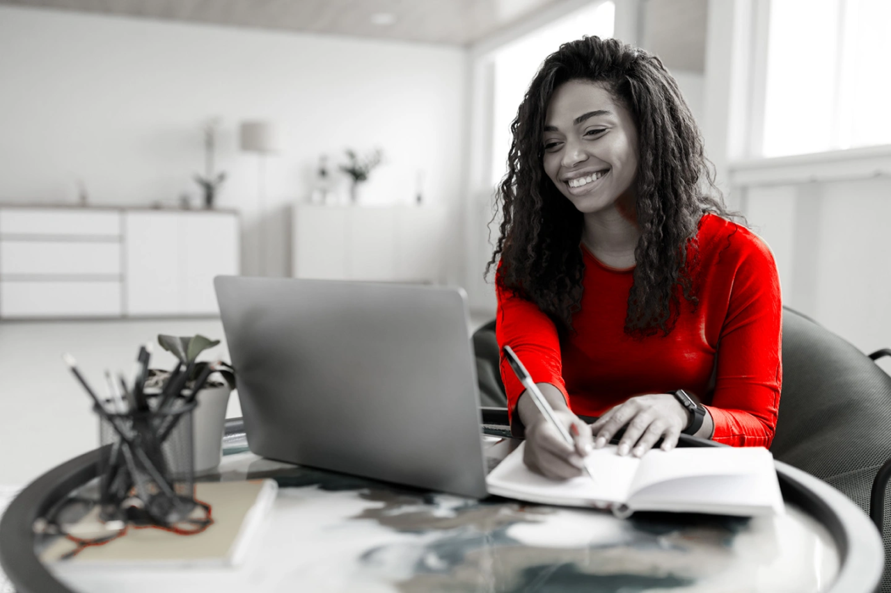 Lady smiling at laptop / making notes.