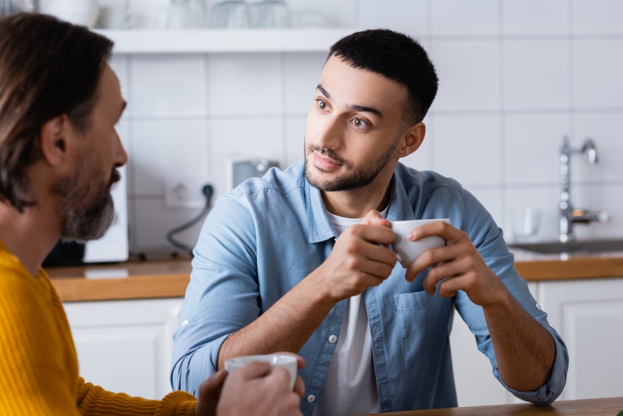 two men talking in the kitchen, one listening intently.